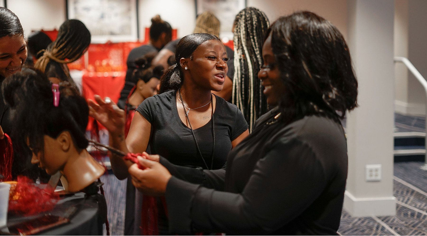 Two braiders working together with red braiding hair