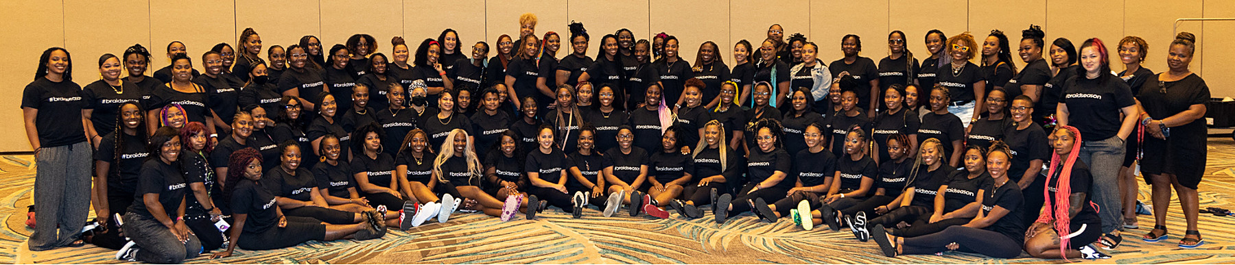 A large group of braiders in matching black shirts on the floor of a ballroom