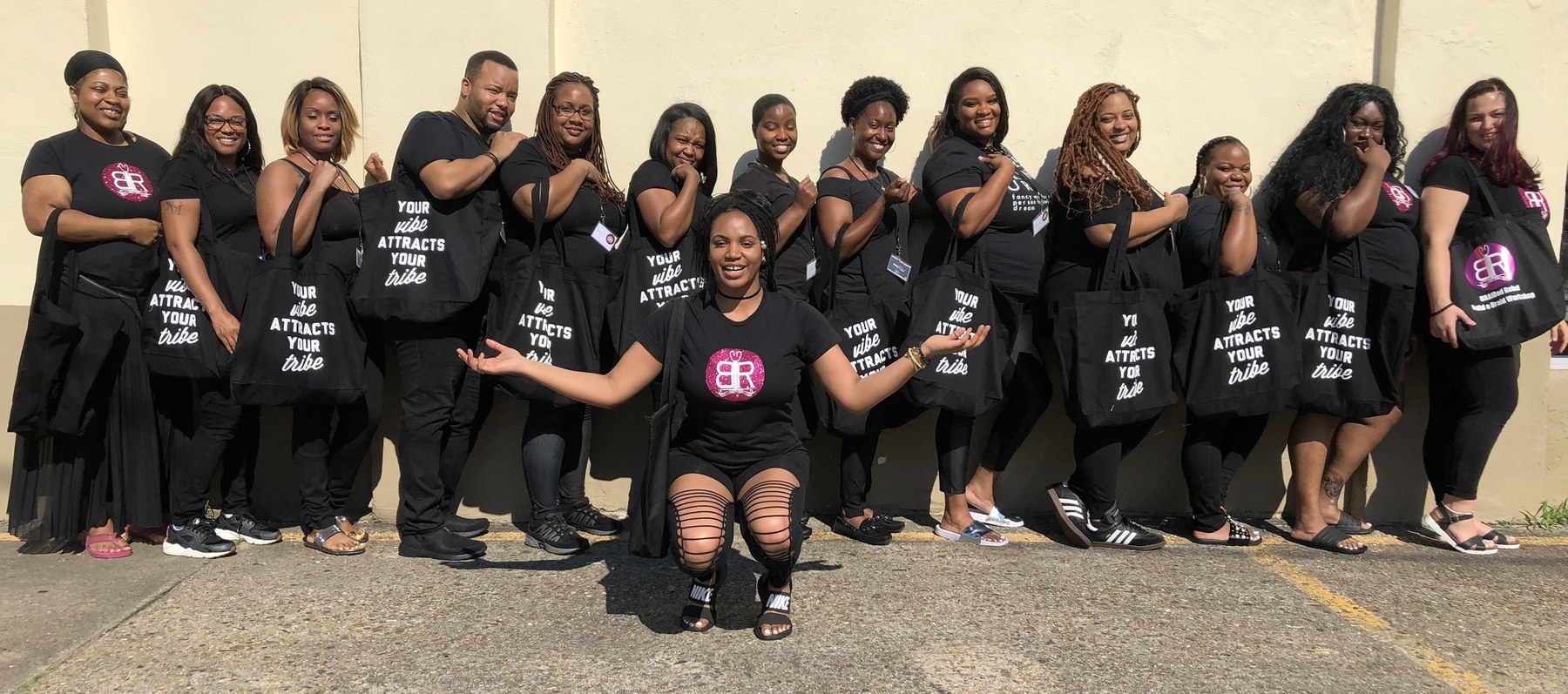 Braiders holding tote bags that read Your vibe attracts your tribe